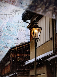 A digital photo depicting a rainy scene of a side of a building with a street lamp as a focal point. In the background handwritten script with the faint image of postal stamps can be seen.